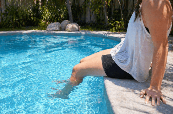 Person sitting on the edge of a swimming pool with one leg in the clear water