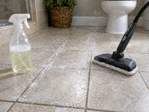 Steam mop and cleaning spray bottle on a bathroom tile floor